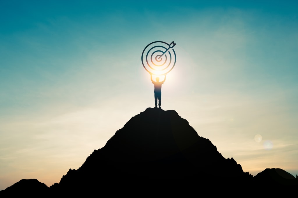 Silhouette of businessman holding target board on the top of mountain symbolizing life achievement